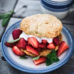 45 degree overhead of vegan strawberry shortcake on a blue and white plate outside on a picnic table