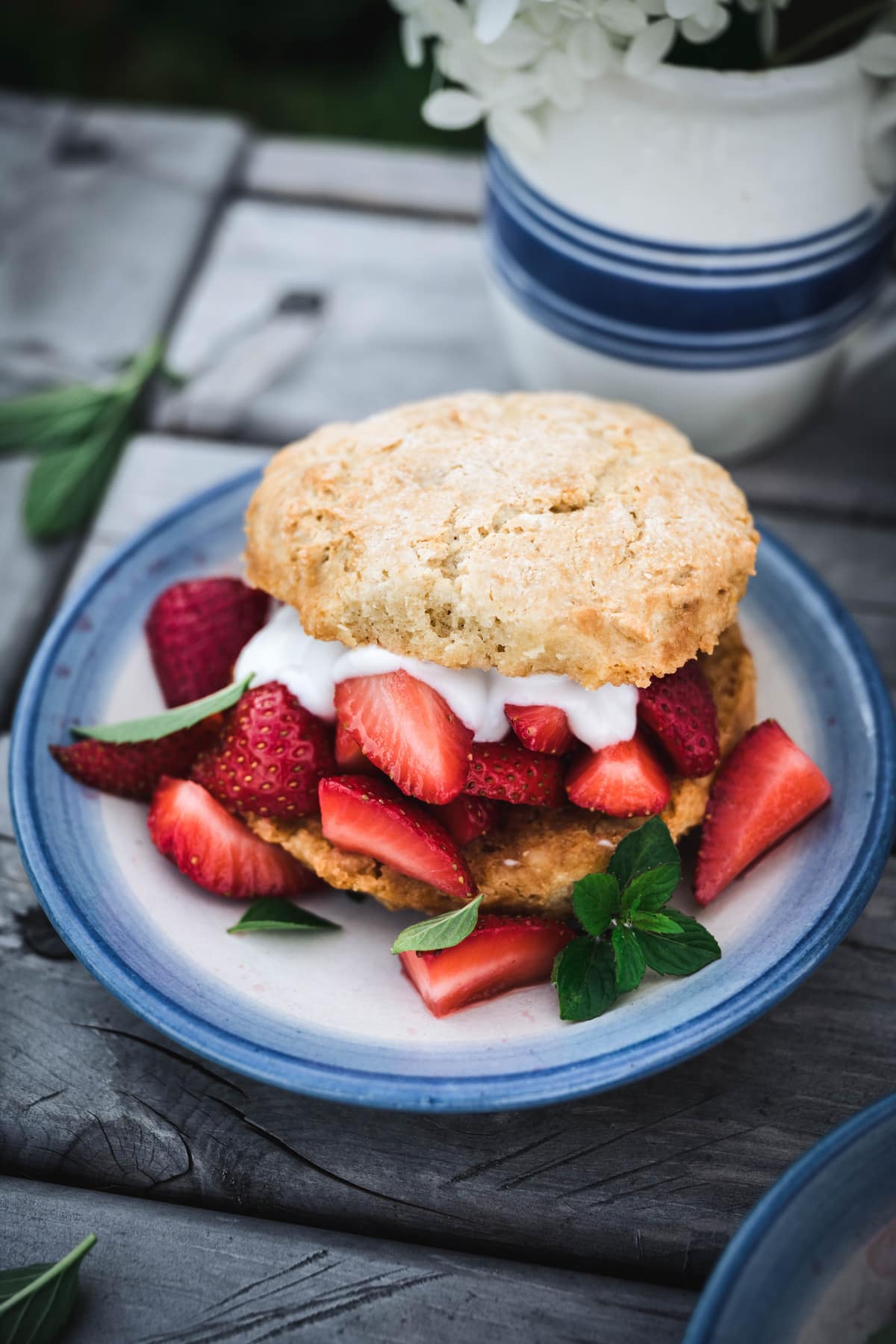 45 degree overhead of vegan strawberry shortcake on a blue and white plate outside on a picnic table