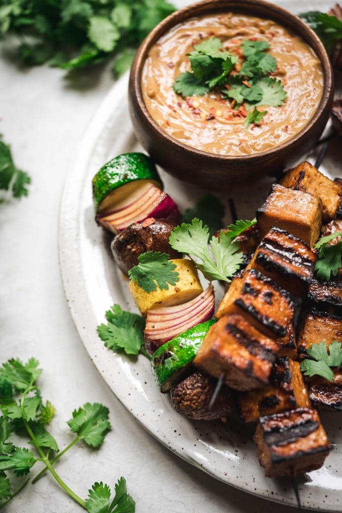overhead of vegan peanut dipping sauce with tofu and vegetable kebabs