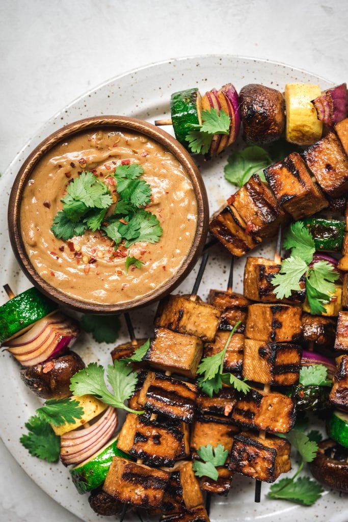 close up on vegan peanut sauce with tofu and vegetable kebabs on a plate