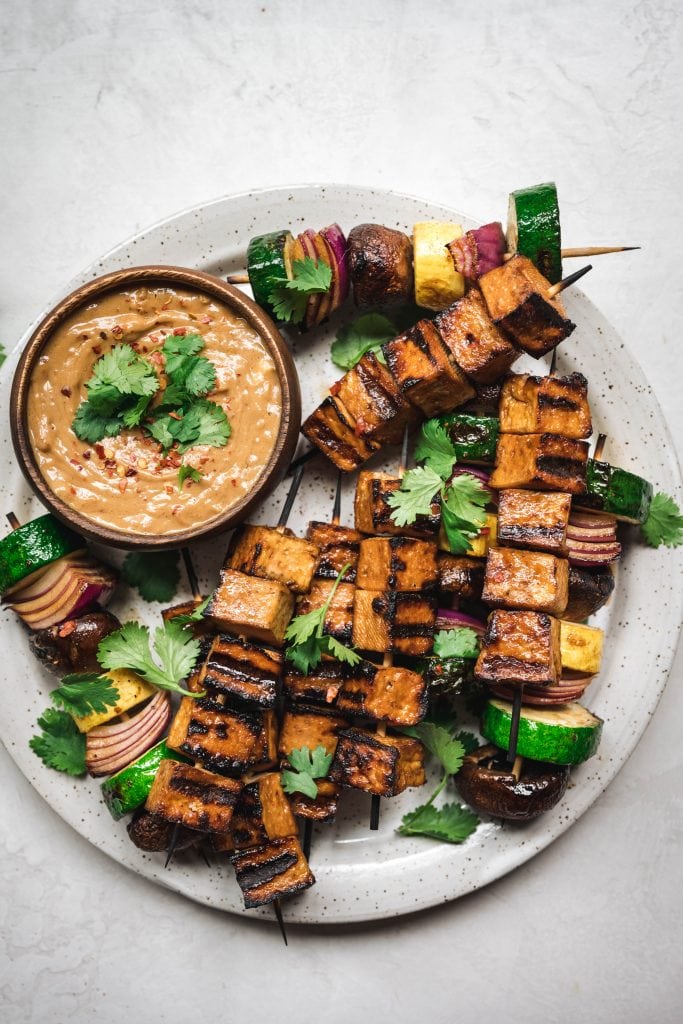 overhead of grilled tofu and vegetable kebabs with peanut sauce