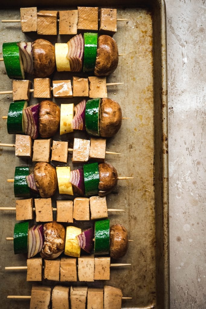 overhead of 10 skewers of marinaded tofu cubes and vegetables on a baking sheet before grilling