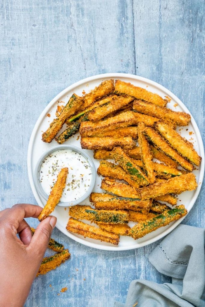 overhead of someone taking an airfryer zucchini fry from a plate