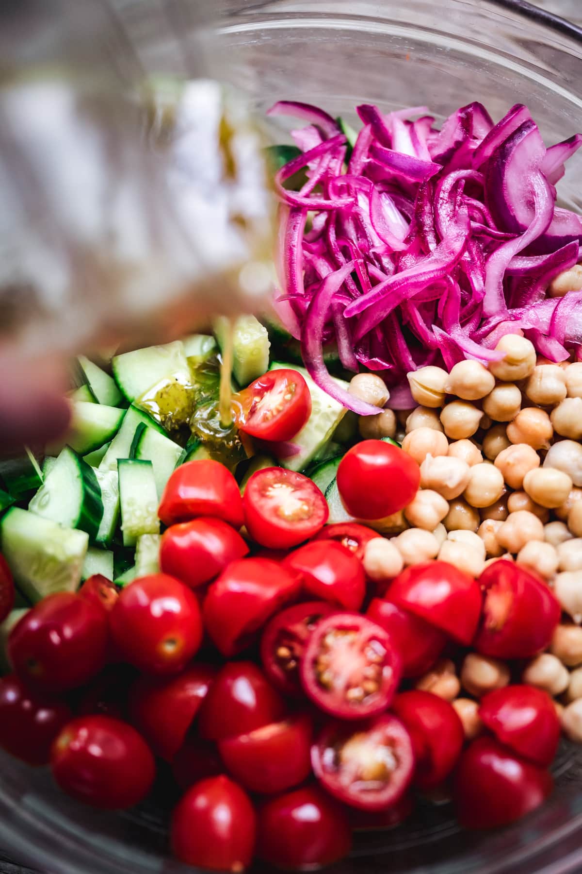 close up of pouring herby vinagrette over vegan cucumber chickpea salad