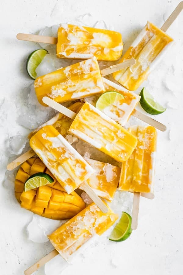 overhead of vegan mango lassi popsicles with mangos and limes on ice