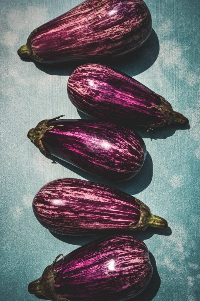 overhead of sciciian eggplants in a row on a blue background