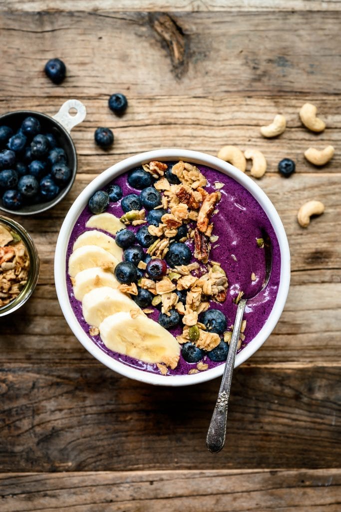 overhead of blueberry recovery smoothie bowl with banana, almond butter and granola
