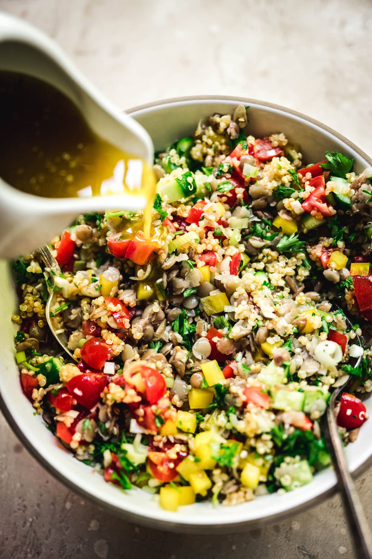 pouring sumac dressing onto a mediterranean quinoa salad