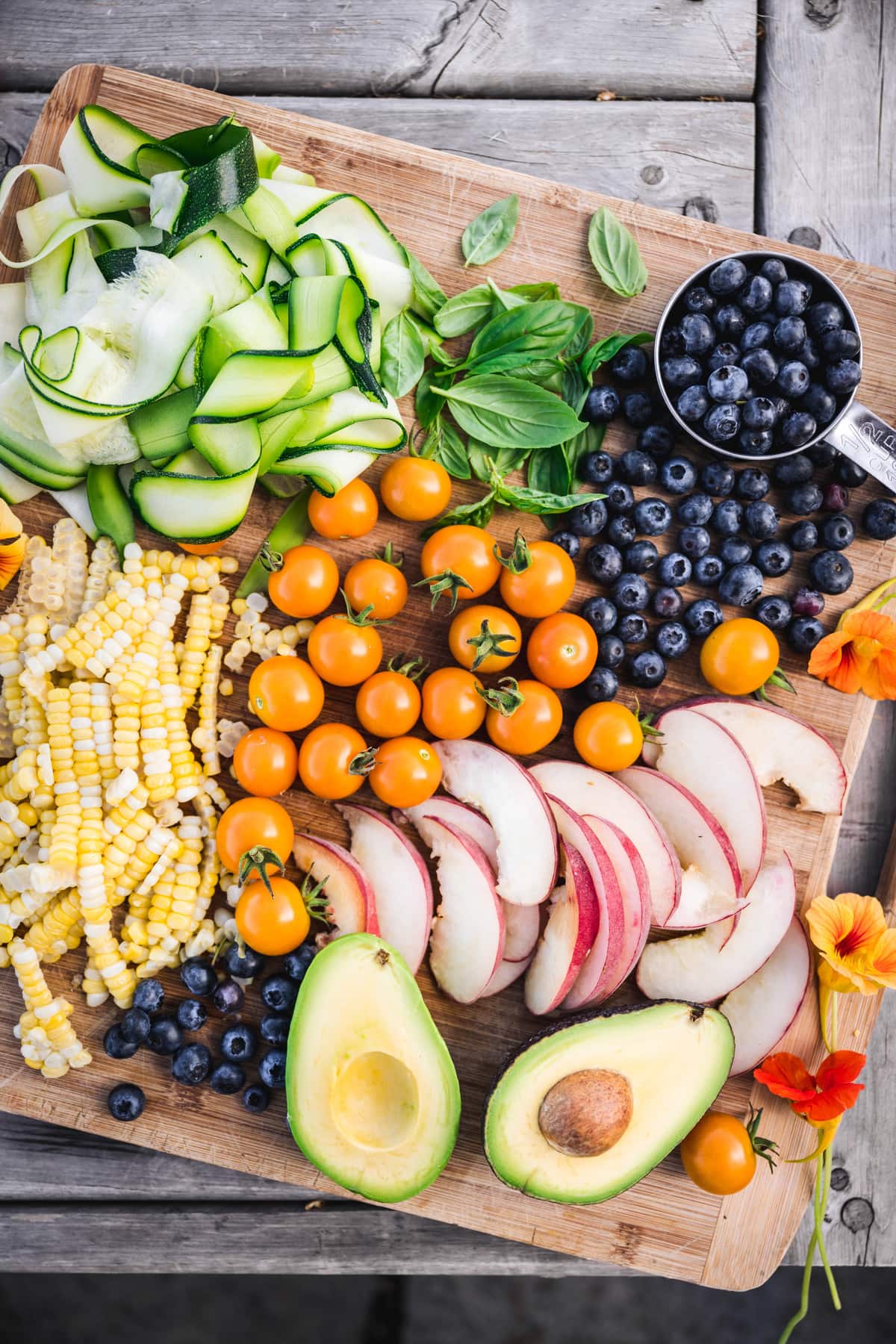 overhead of a wooden cutting board with fresh summer fruits and vegetables