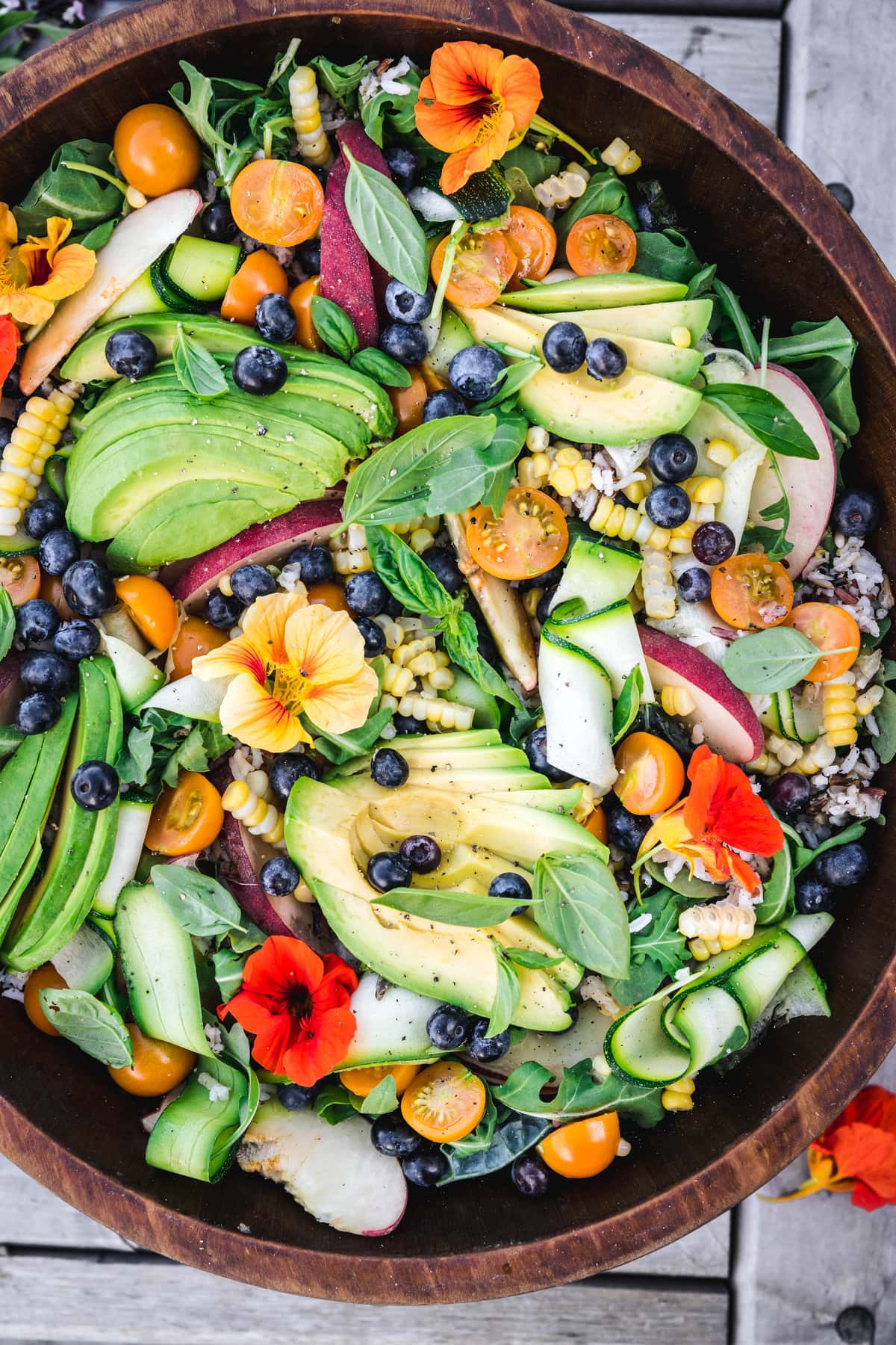 overhead close up of grain salad with fruits and vegetables in a wooden bowl outside