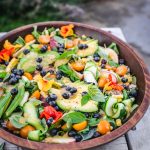 45 degree angle of summer grain salad in a wooden bowl on a picnic table outside