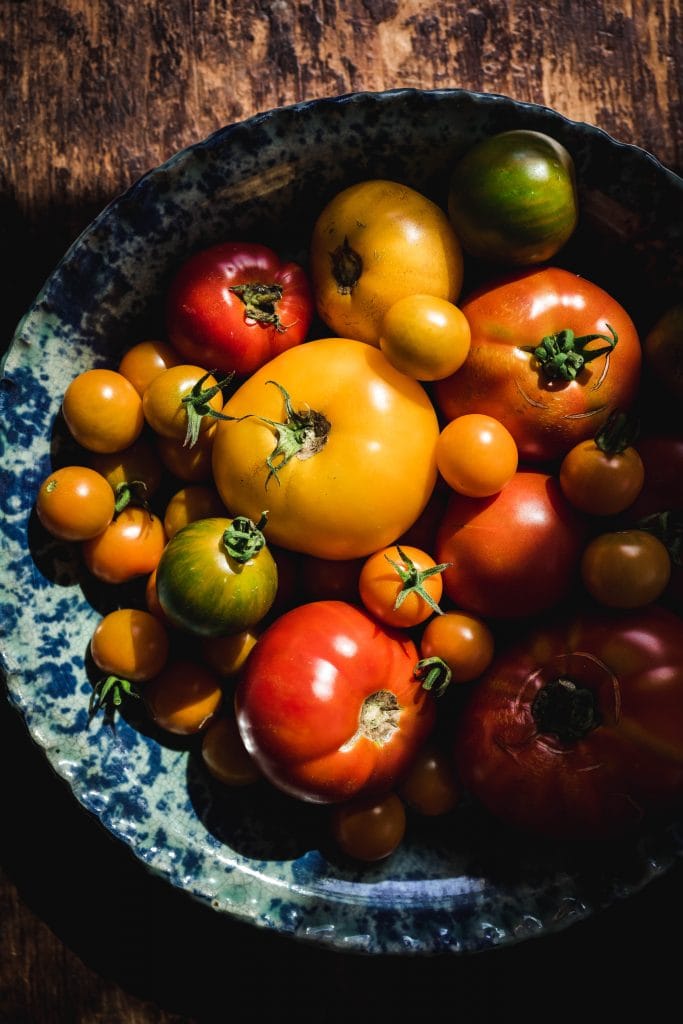 overhead of red yellow green and orange homegrown tomatoes in a speckled pie dish