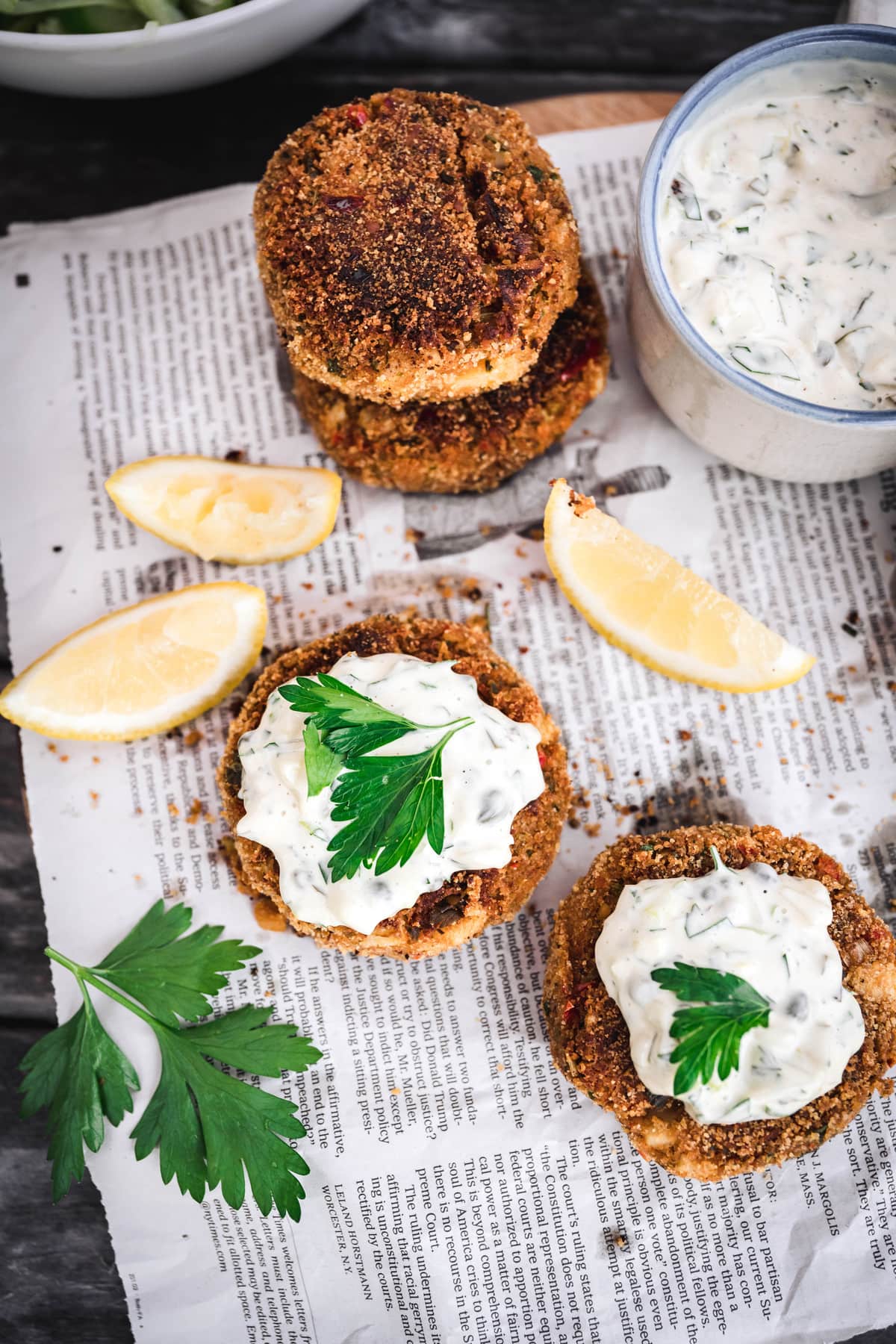 overhead of two vegan crab cakes with vegan tartar sauce on newspaper