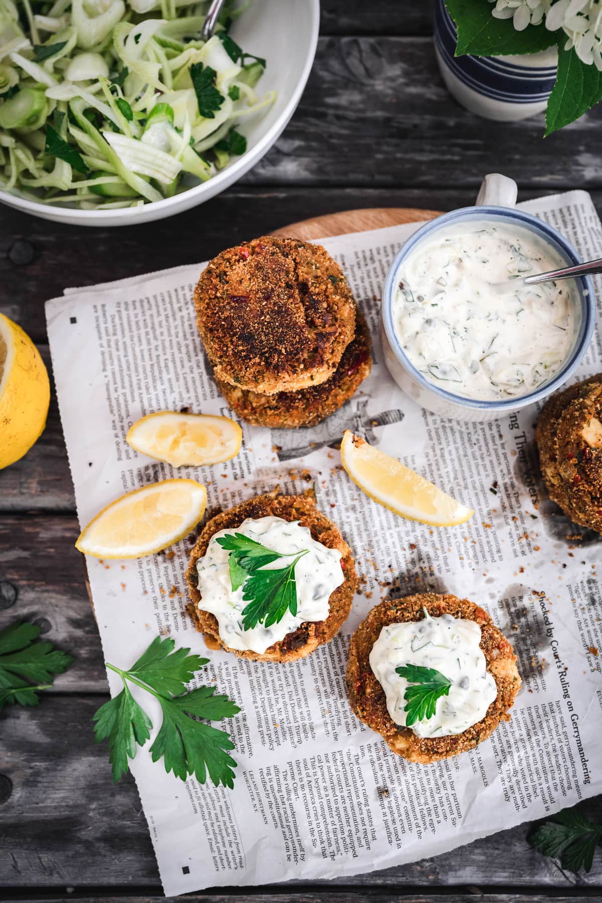 overhead of vegan crab cakes with vegan tartar sacue on newspaper and a fennel salad