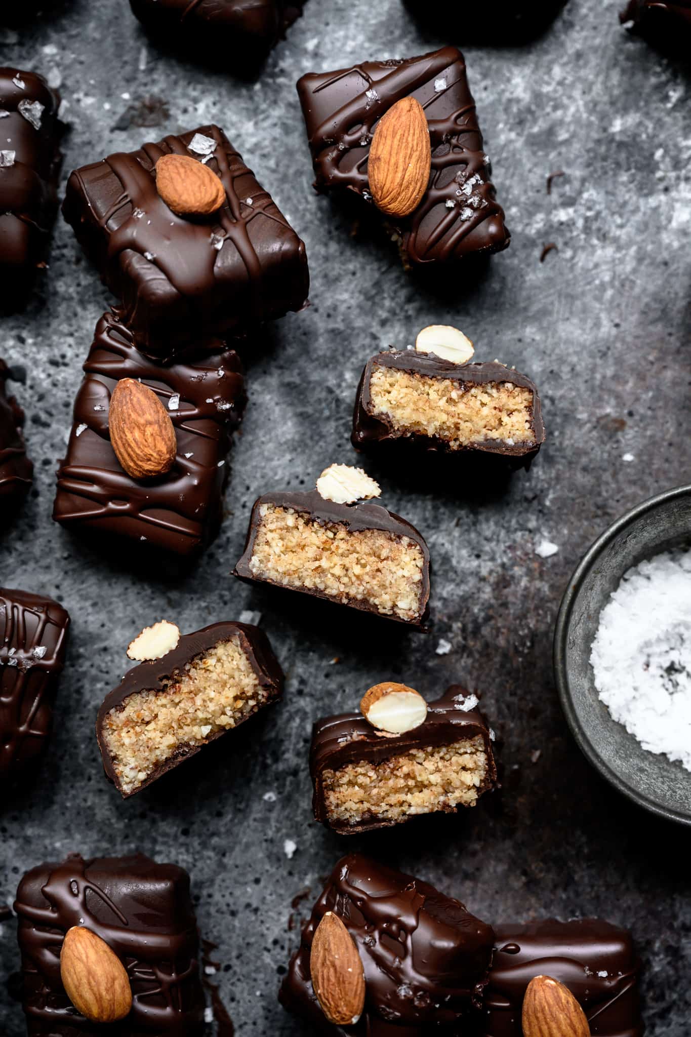 overhead of homemade vegan almond joy bars on a dark stone background cut open so you can see the creamy filling