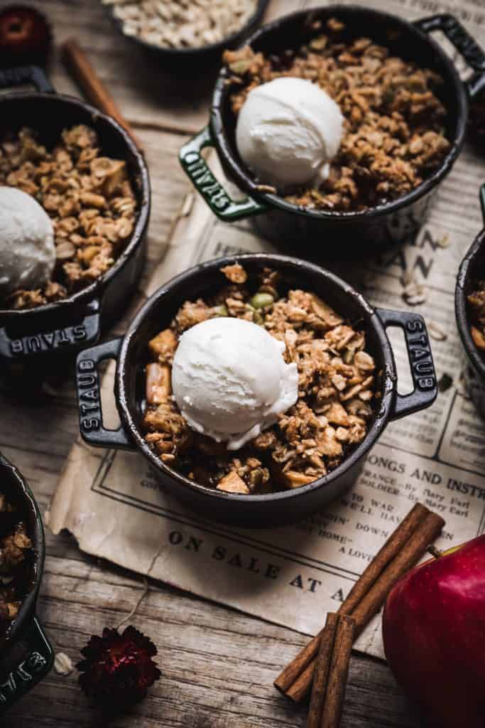 overhead of mini vegan apple crisps in ramekins with vanilla ice cream on top