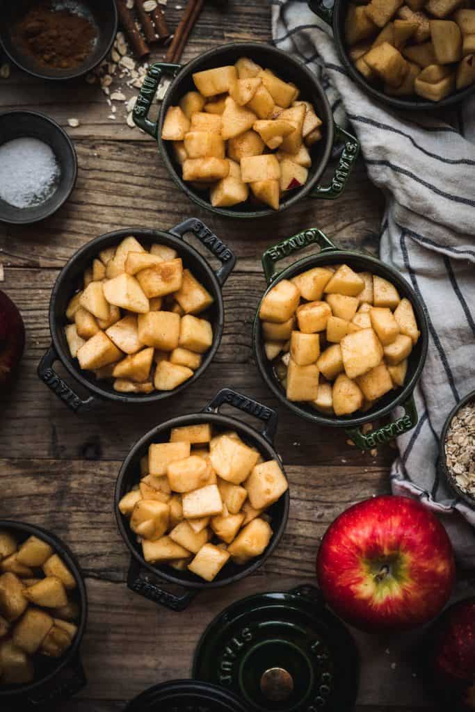 overhead of four cast iron ramekins with seasoned apples for vegan apple crisp