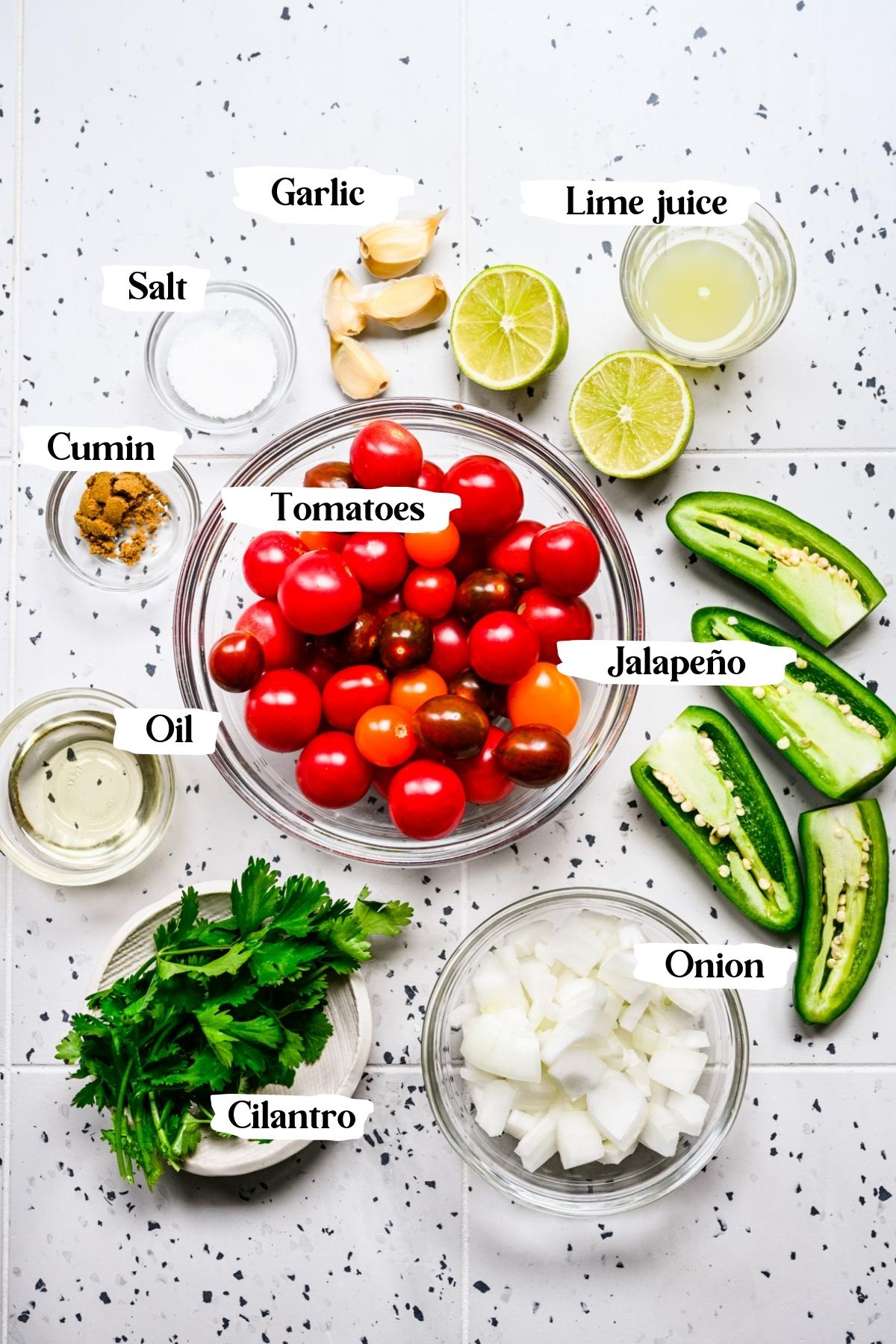 Overhead view of ingredients for cherry tomato salsa in small prep bowls. 