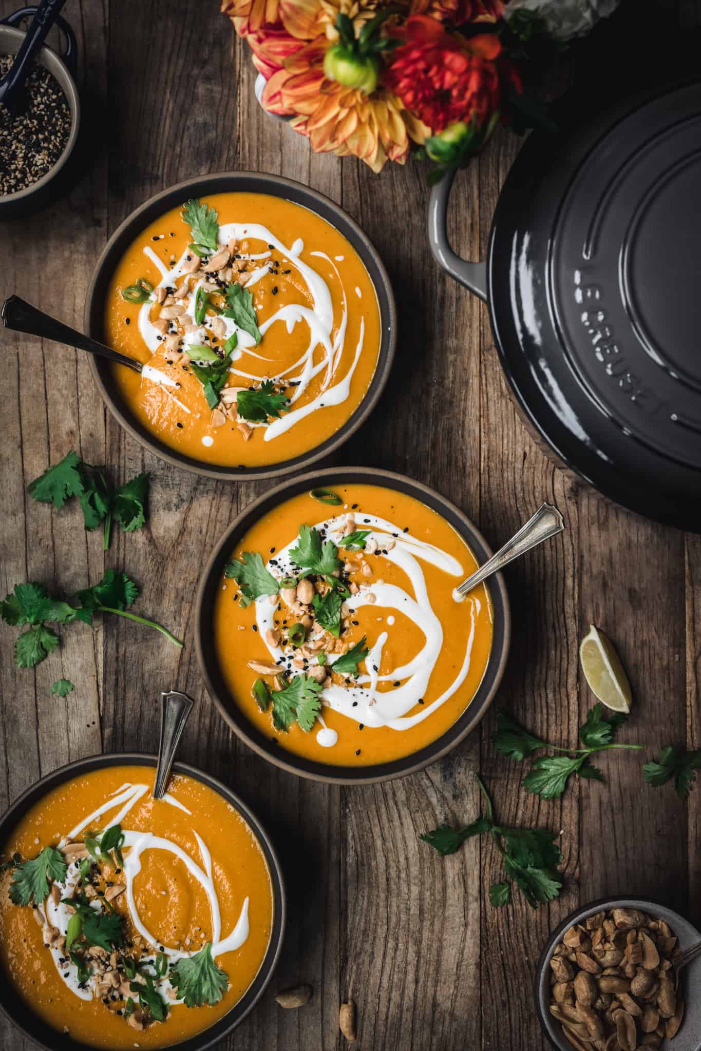 overhead view of three bowls of vegan butternut squash soup on a wood background