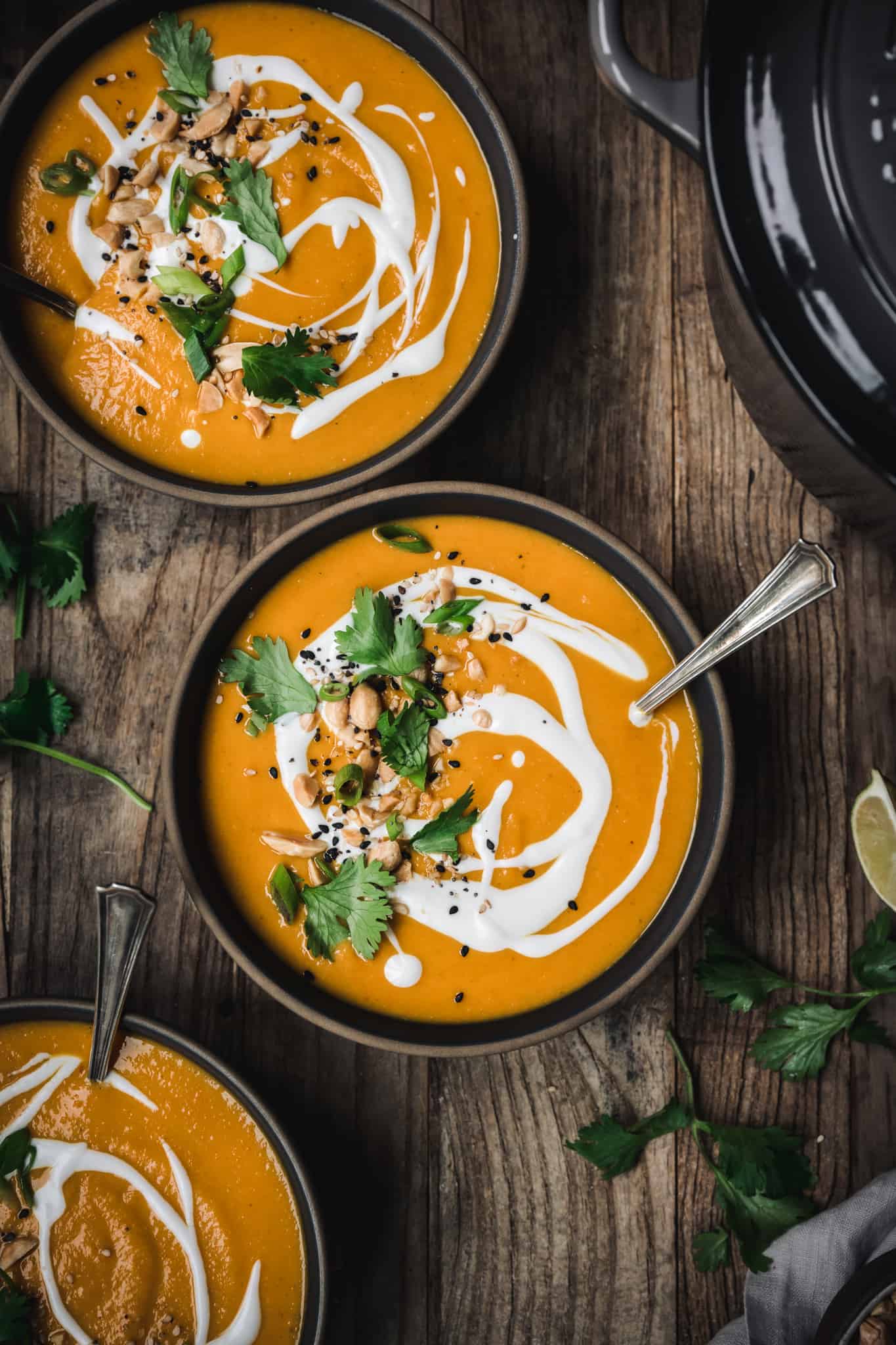 overhead view of coconut curry butternut squash soup garnished with coconut milk and cilantro on wood background