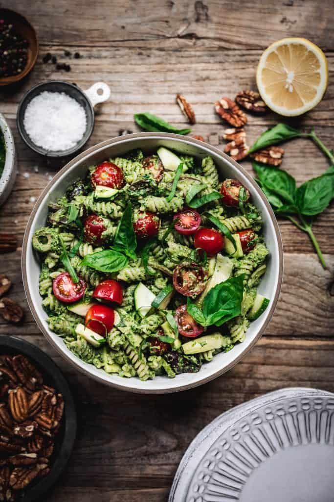 overhead view of pesto pasta salad with summer vegetables in white bowl