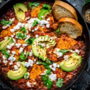 Tofu shakshuka in a cast iron skillet garnished with feta and avocado.