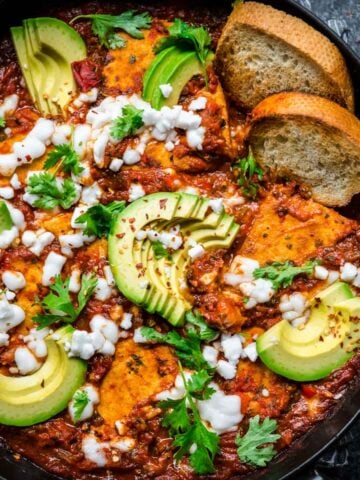 Tofu shakshuka in a cast iron skillet garnished with feta and avocado.