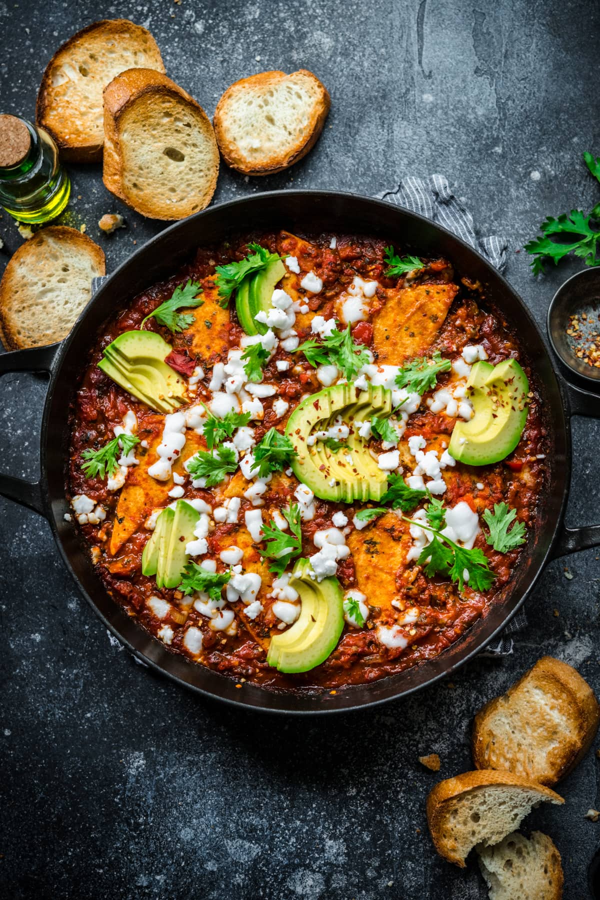 Vegan shakshuka in a cast iron skillet with parsley, vegan feta, and avocados for garnish.