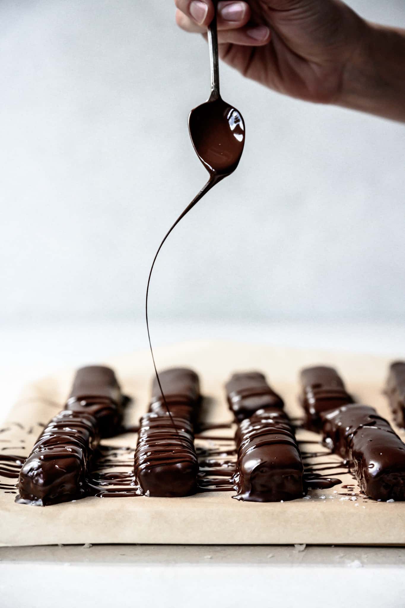 Action shot of person drizzling dark chocolate onto homemade Twix bars