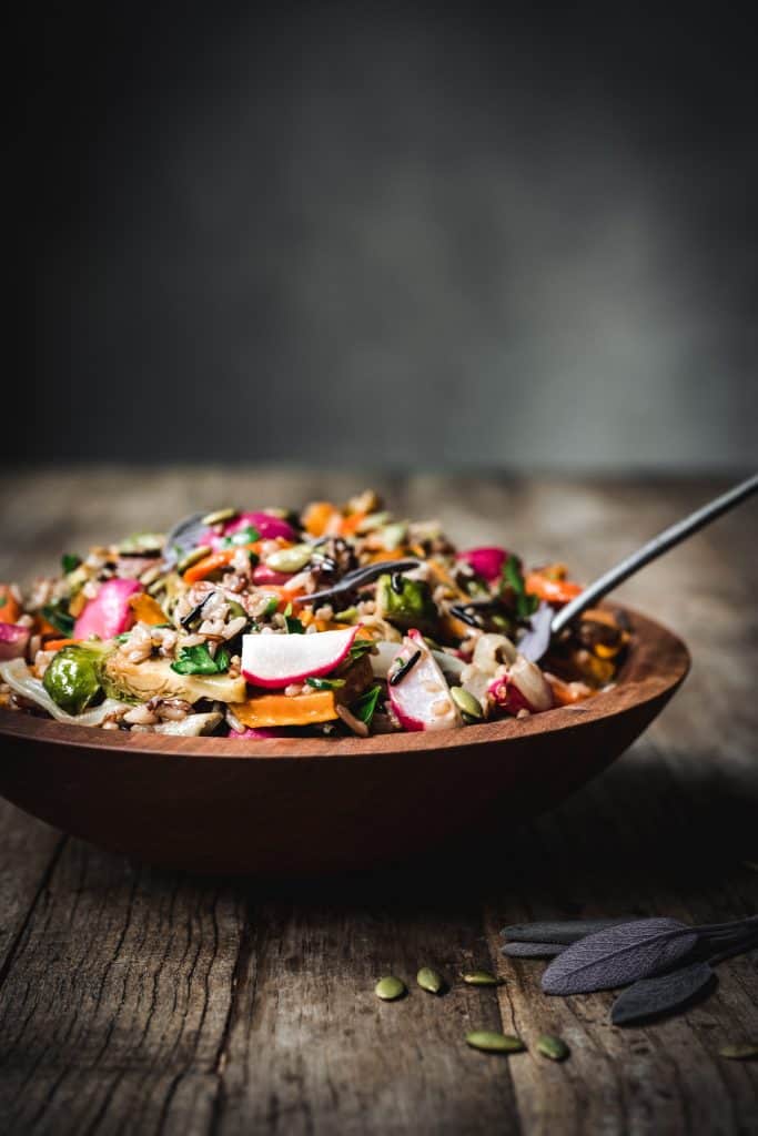 side view of a woooden bowl with harvest salad and a fork