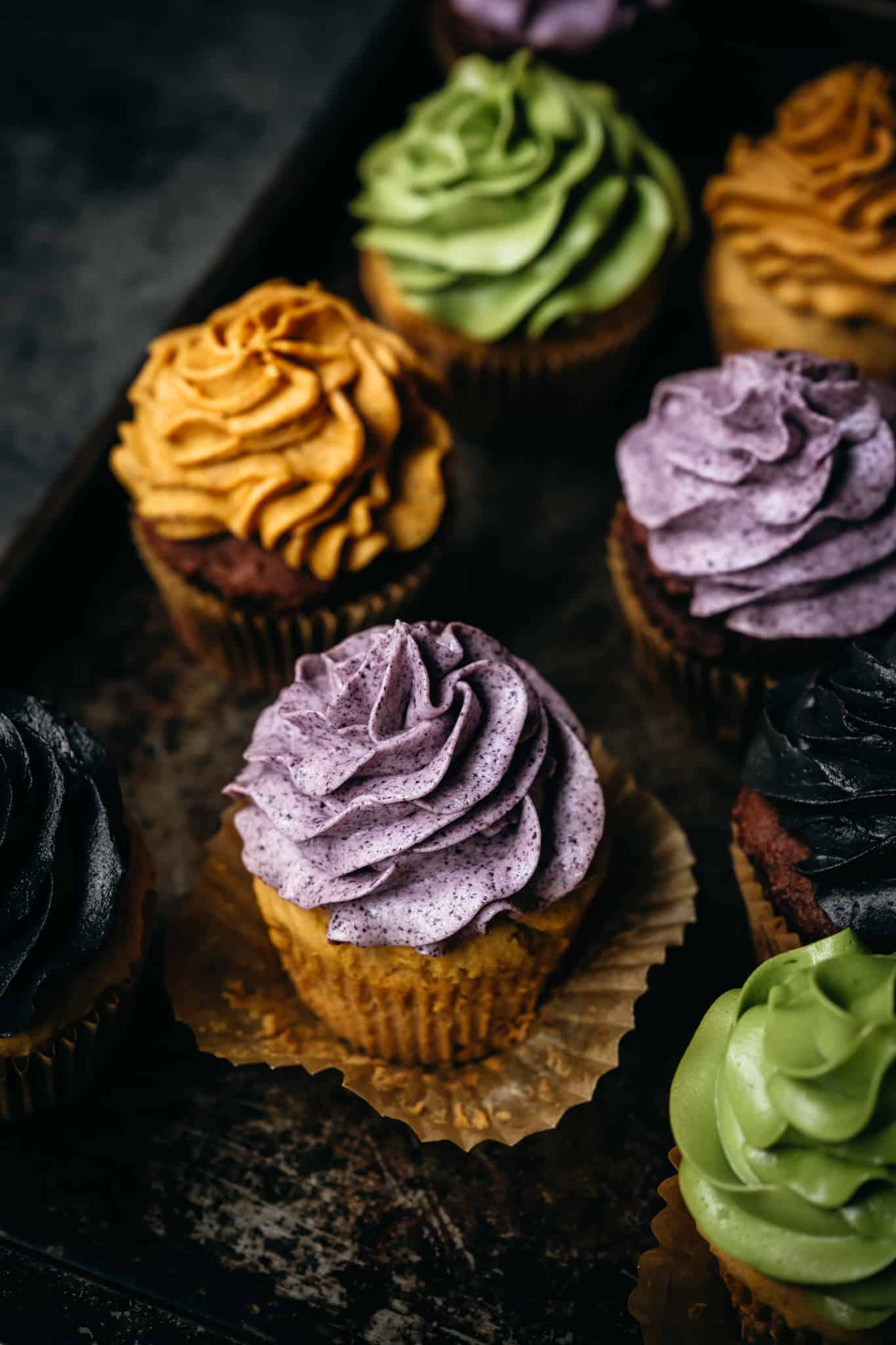 45 degree overhead of vegan cupcakes with naturally dyed buttercream frosting in purple, yellow and green