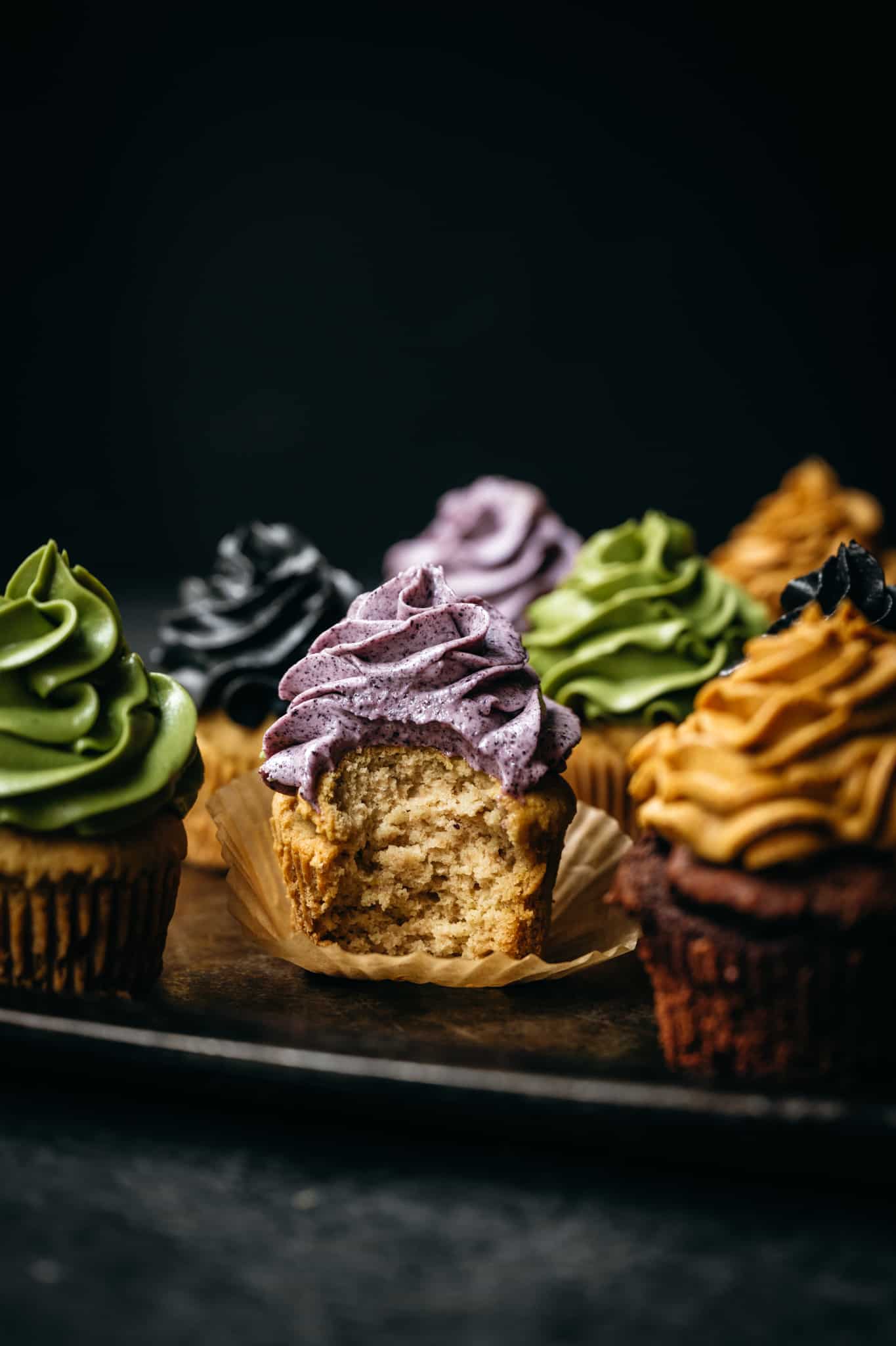 close up of vegan cupcakes topped with buttercream dyed with natural vegan food colorings with a bite taken out