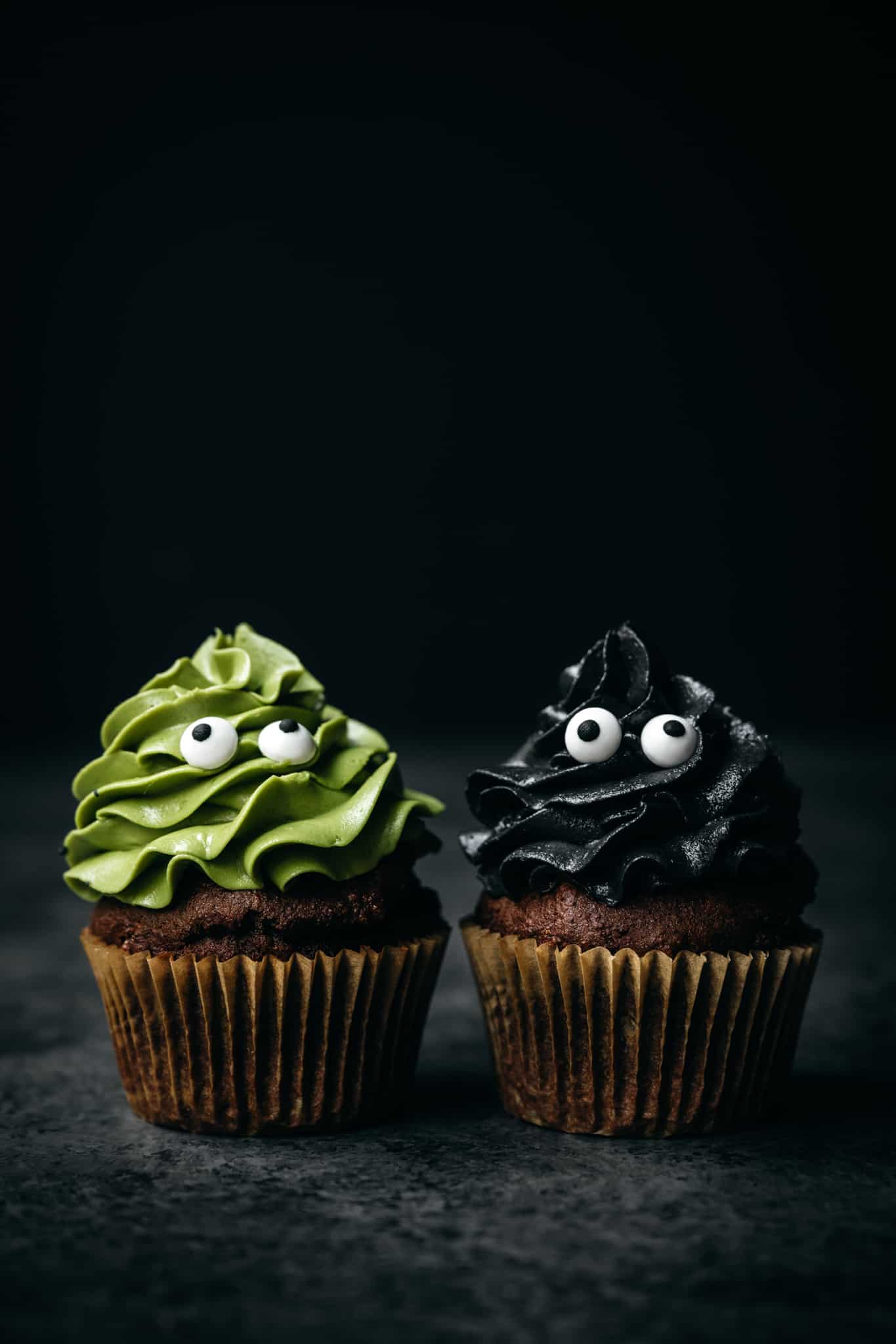side view of two vegan chocolate cupcakes topped with naturally colored frosting in green and black from charcoal