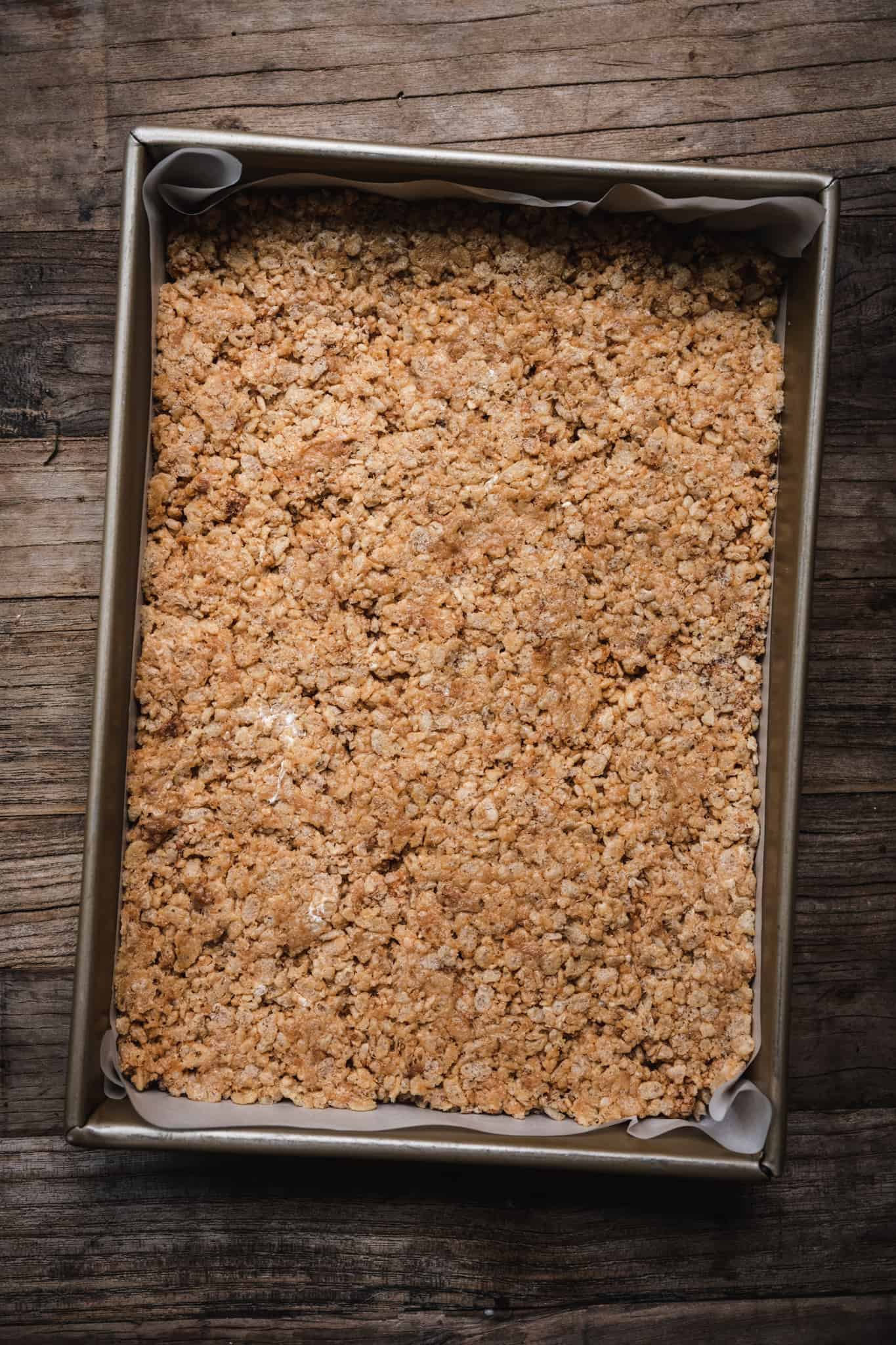 overhead of vegan peanut butter rice krispy dough pressed into a prepared baking dish