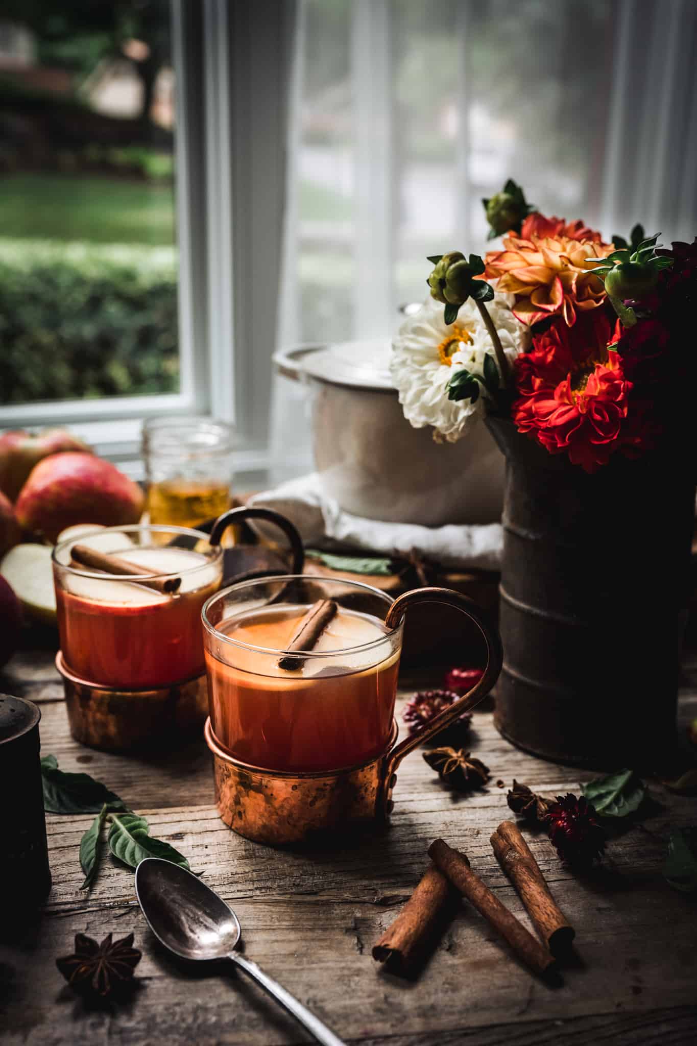 backlit side view of hot apple cider brandy cocktails with beautiful fall flowers