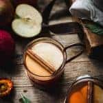 Overhead view of hot apple cider cocktail garnished with cinnamon stick on rustic wood background