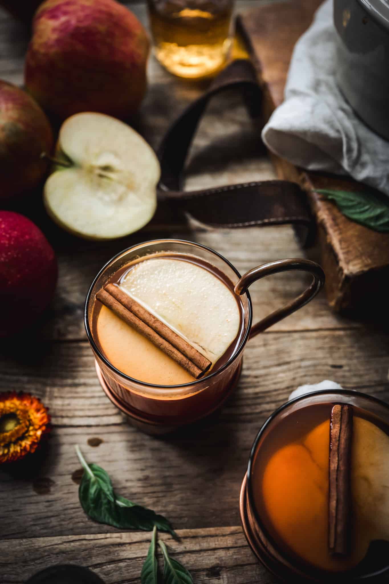 Overhead view of hot apple cider cocktail garnished with cinnamon stick on rustic wood background