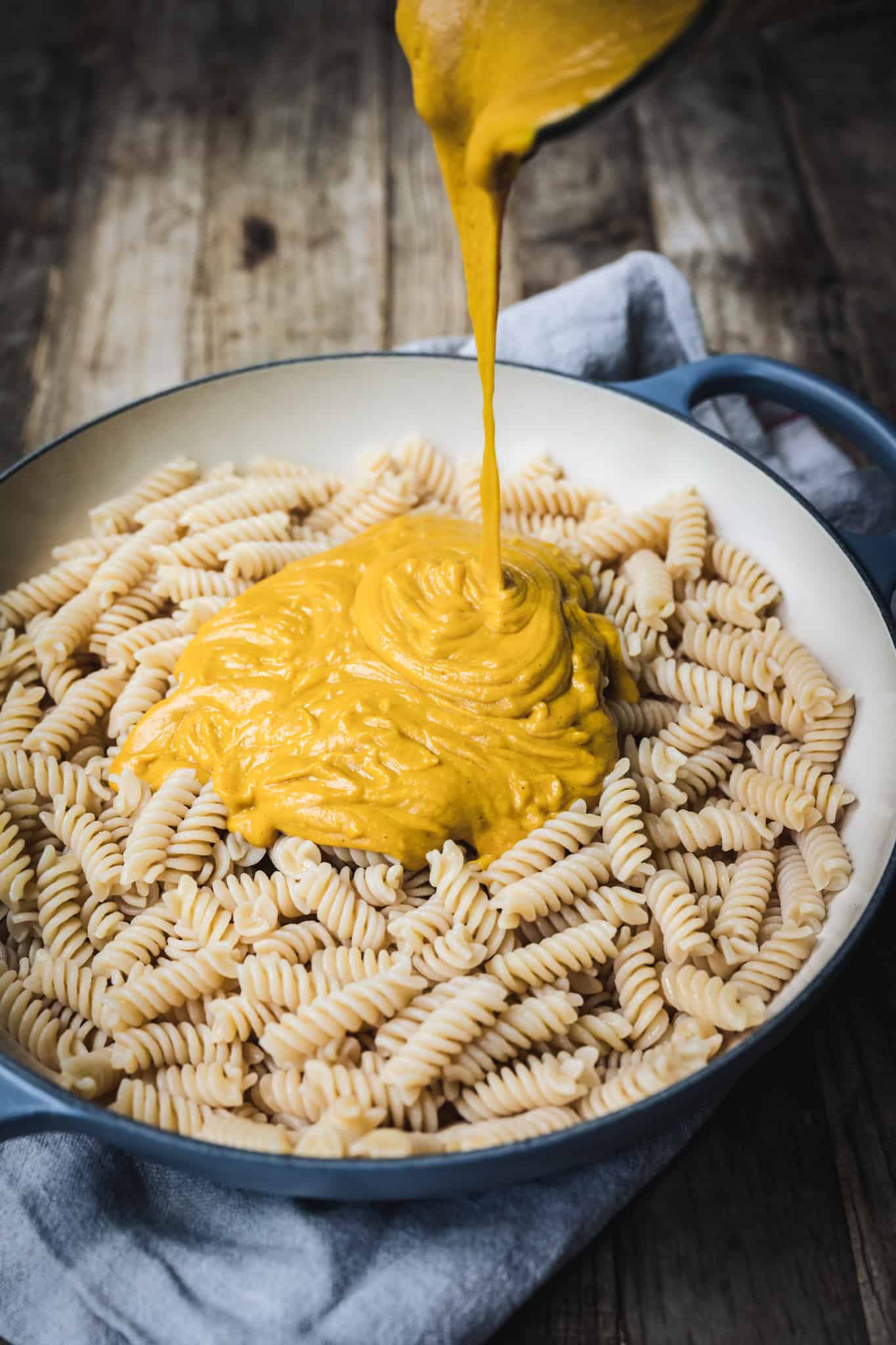 45 degree overhead of pouring vegan cheese sauce over macaroni in a baking dish