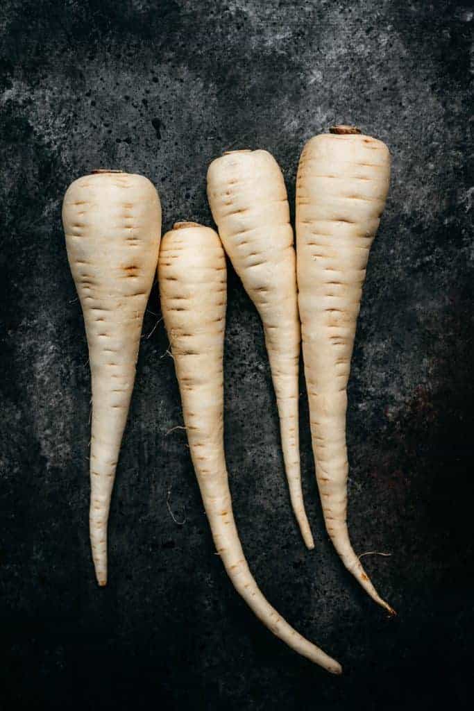 overhead of four white parsnips on a black background