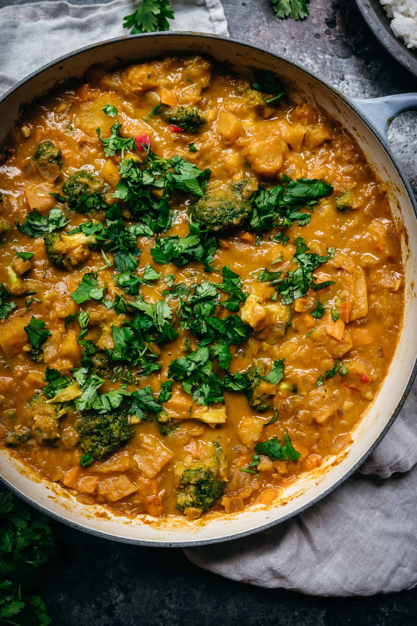 overhead of large pot of vegan pumpkin curry topped with fresh herbs