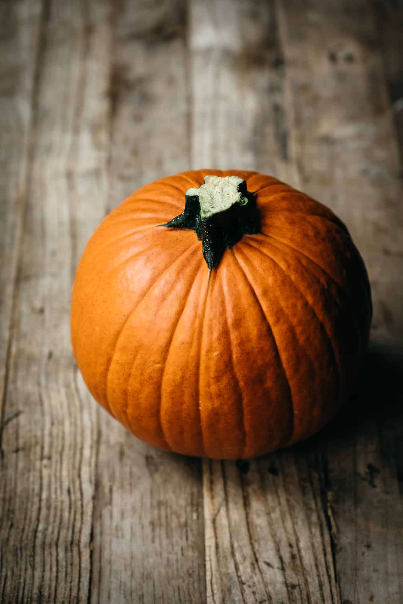 45 degree overhead of a small orange pumpkin on a wooden table top background