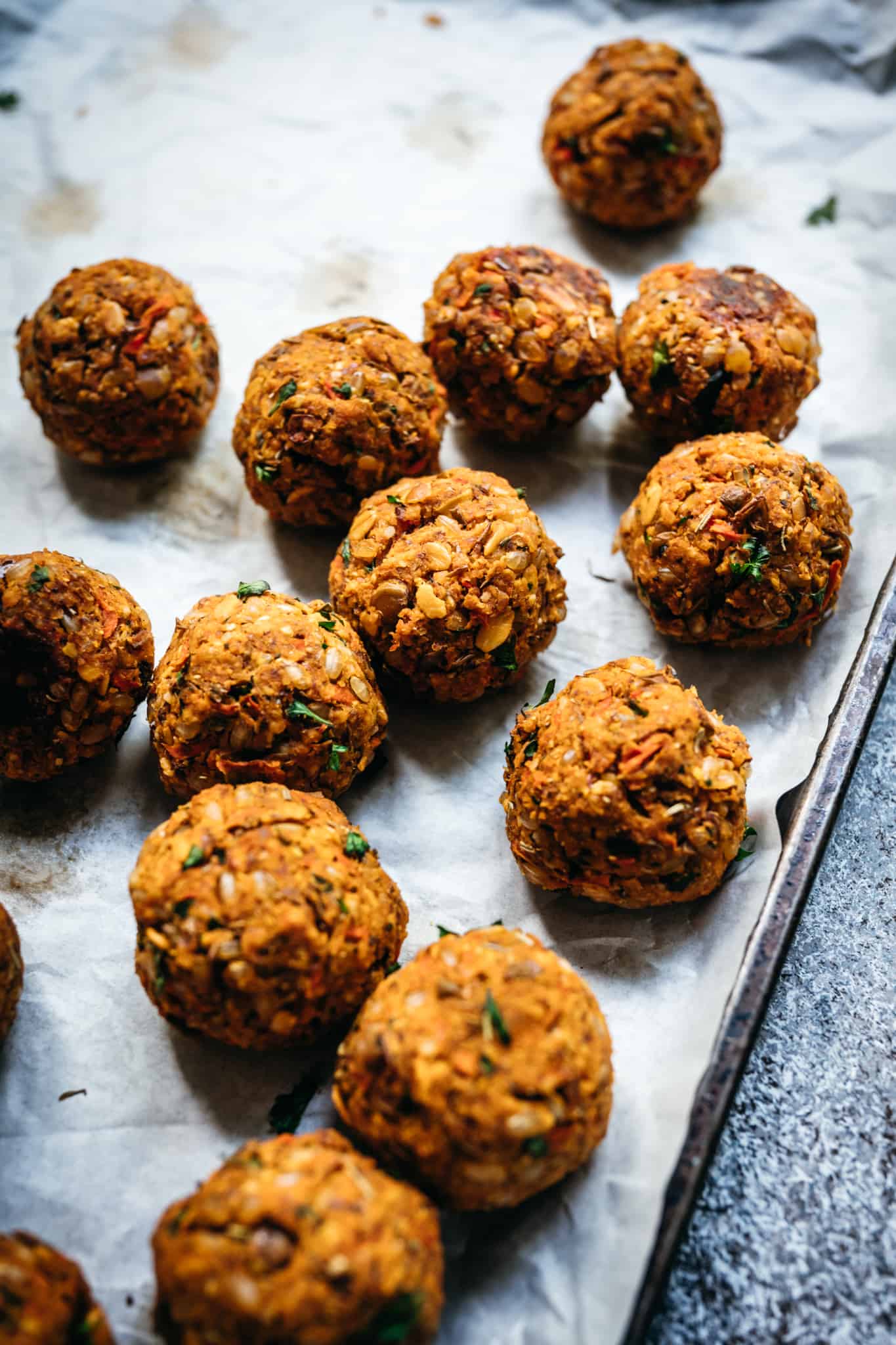 close up of shaped vegan lentil meatballs on a parchment paper lined baking sheet