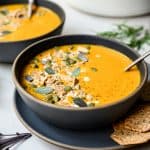 side view of vegan carrot apple soup in a grey bowl with spoon