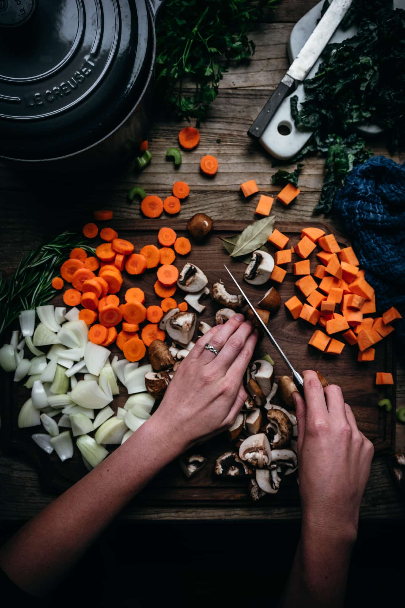 overhead view of person cutting mushrooms and other fall vegetables on a wood cutting board