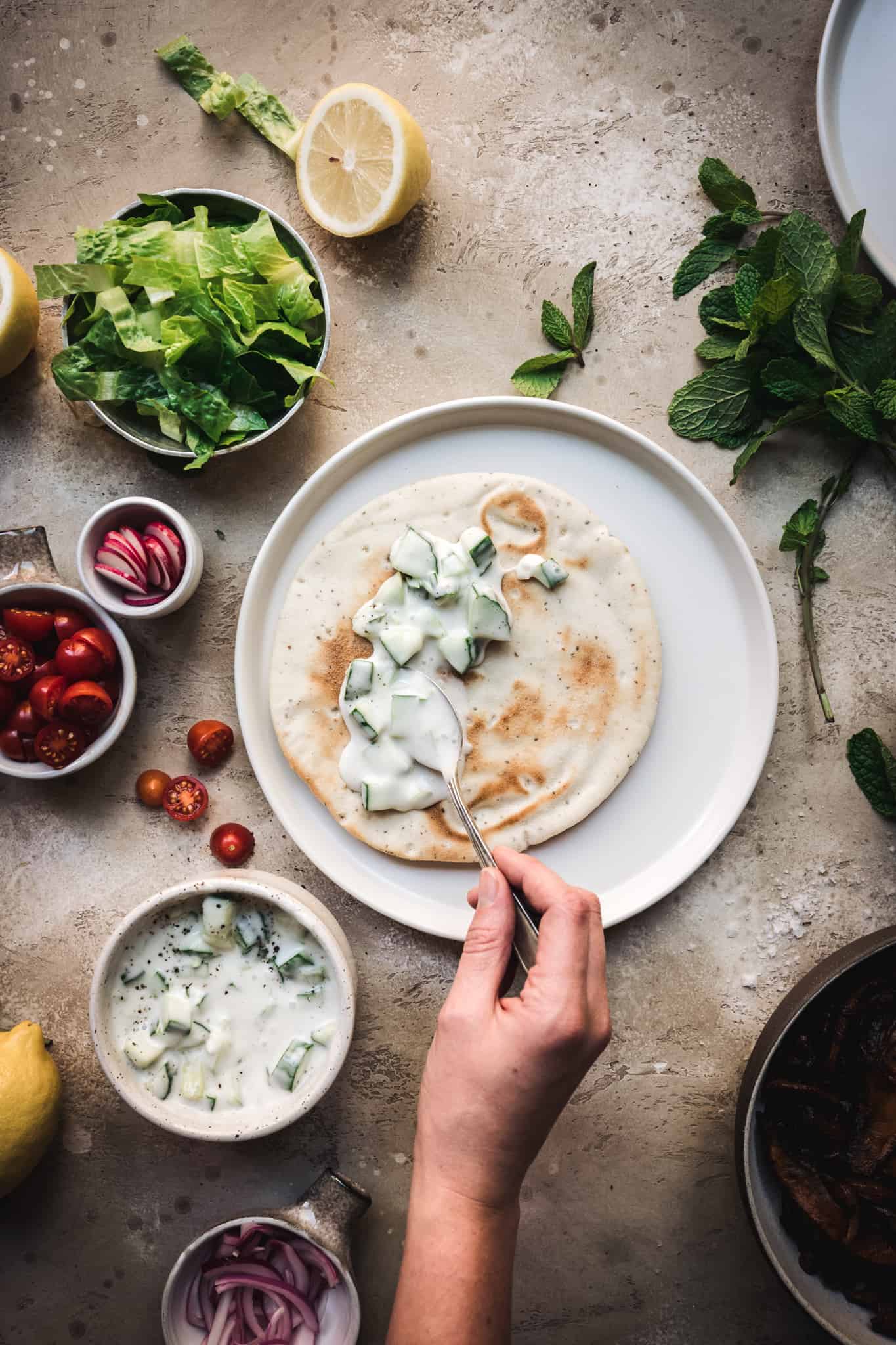 overhead view of spreading vegan tzatziki sauce onto a pita