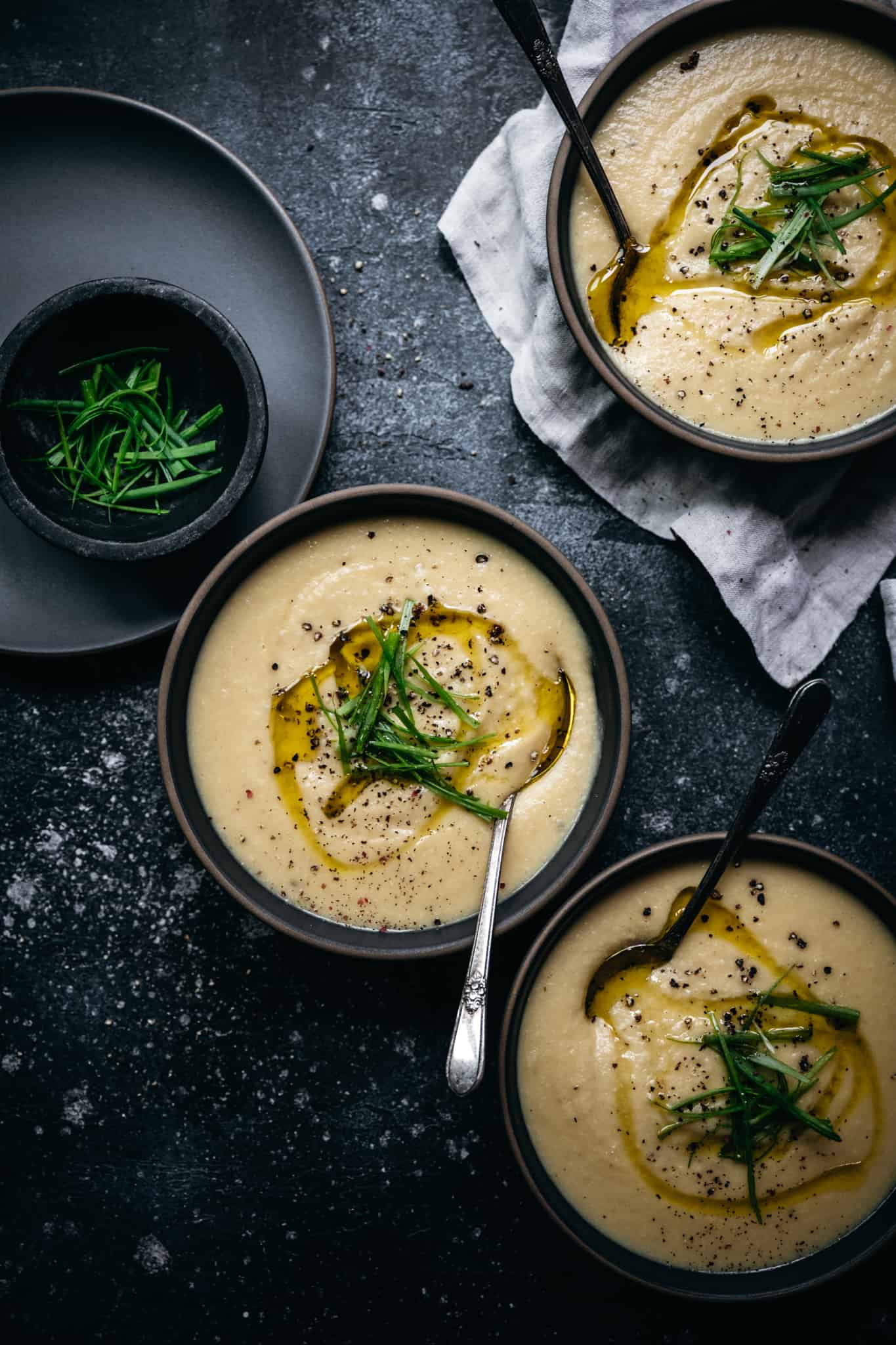 overhead view of 3 bowls of vegan cauliflower and potato soup topped with scallions and olive oil