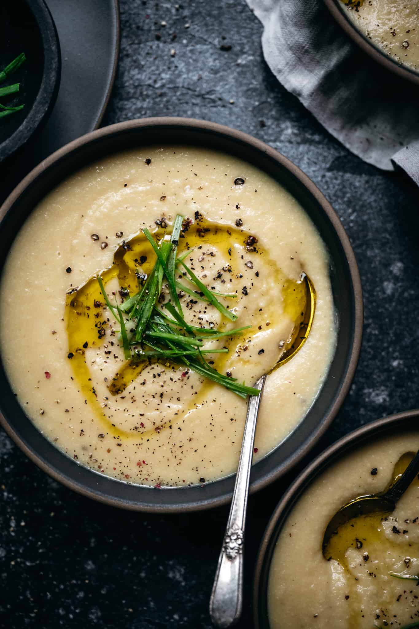 overhead view of 1 bowl of vegan cauliflower and potato soup topped with scallions and olive oil