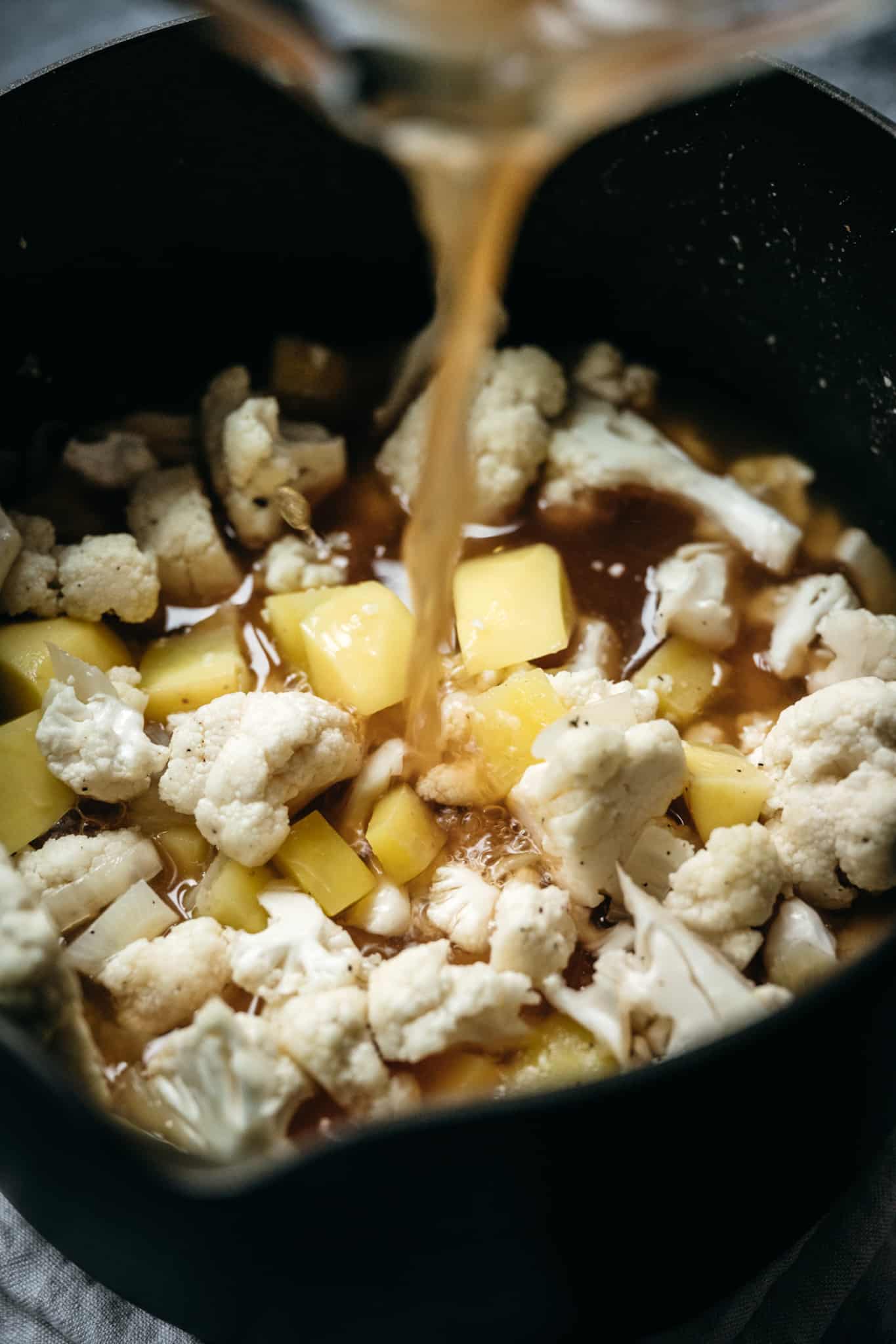 Pouring vegetable broth into cauliflower potato soup