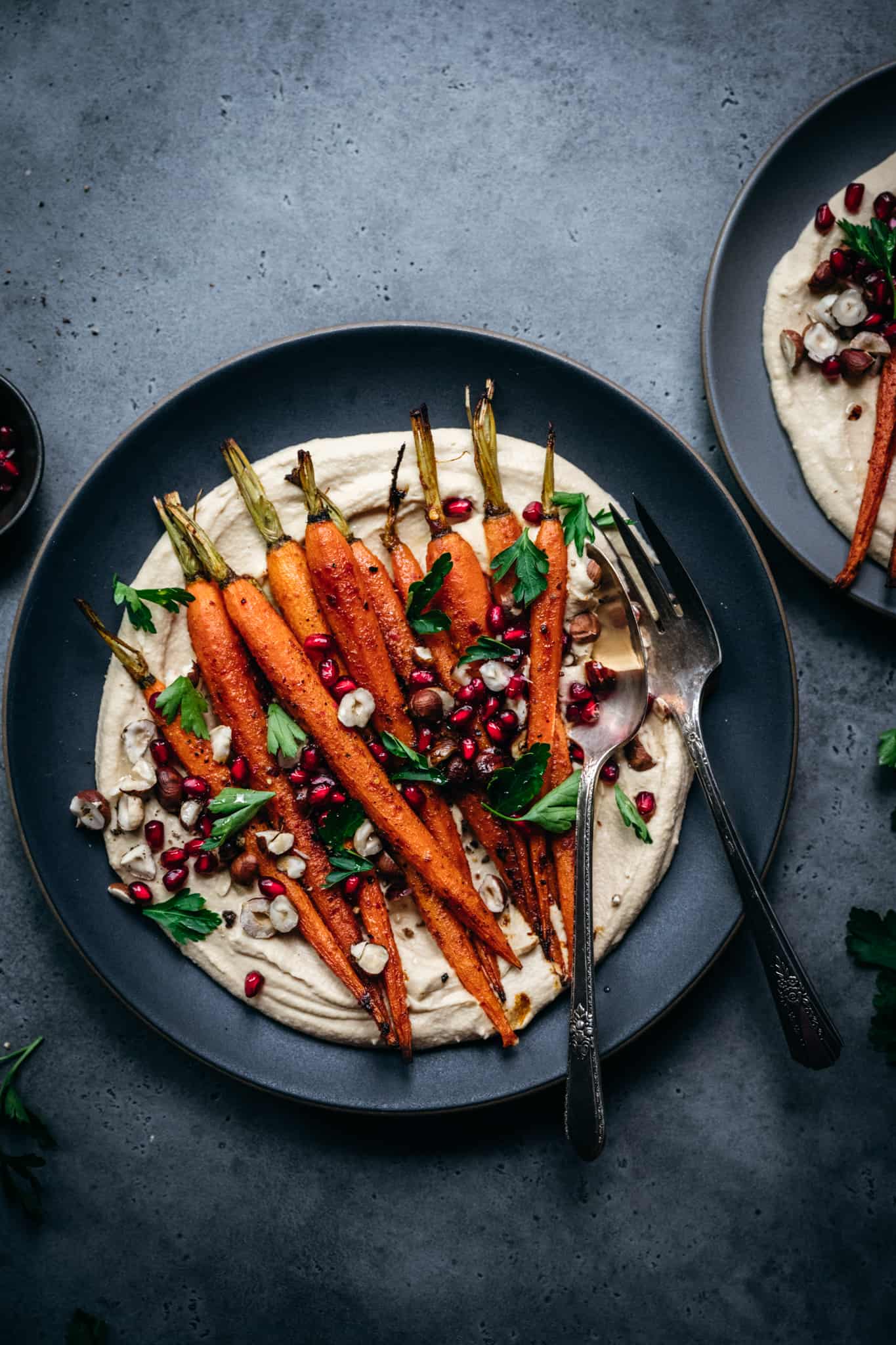 overhead of harissa roasted crrots on a bed of pumpkin humms on a black plate