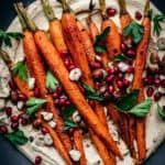 close up overhead of harissa roasted carrots on pumpkin hummus with pomegranate seeds